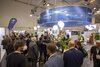 Besucherinnen und Besucher versammeln sich am Stand der Stadt Essen auf einer Messe, umgeben von Informationsmaterialien und Pflanzen.