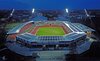 Luftaufnahme eines modernen Stadions mit beleuchteten Tribünen und Solarpaneelen auf dem Dach.